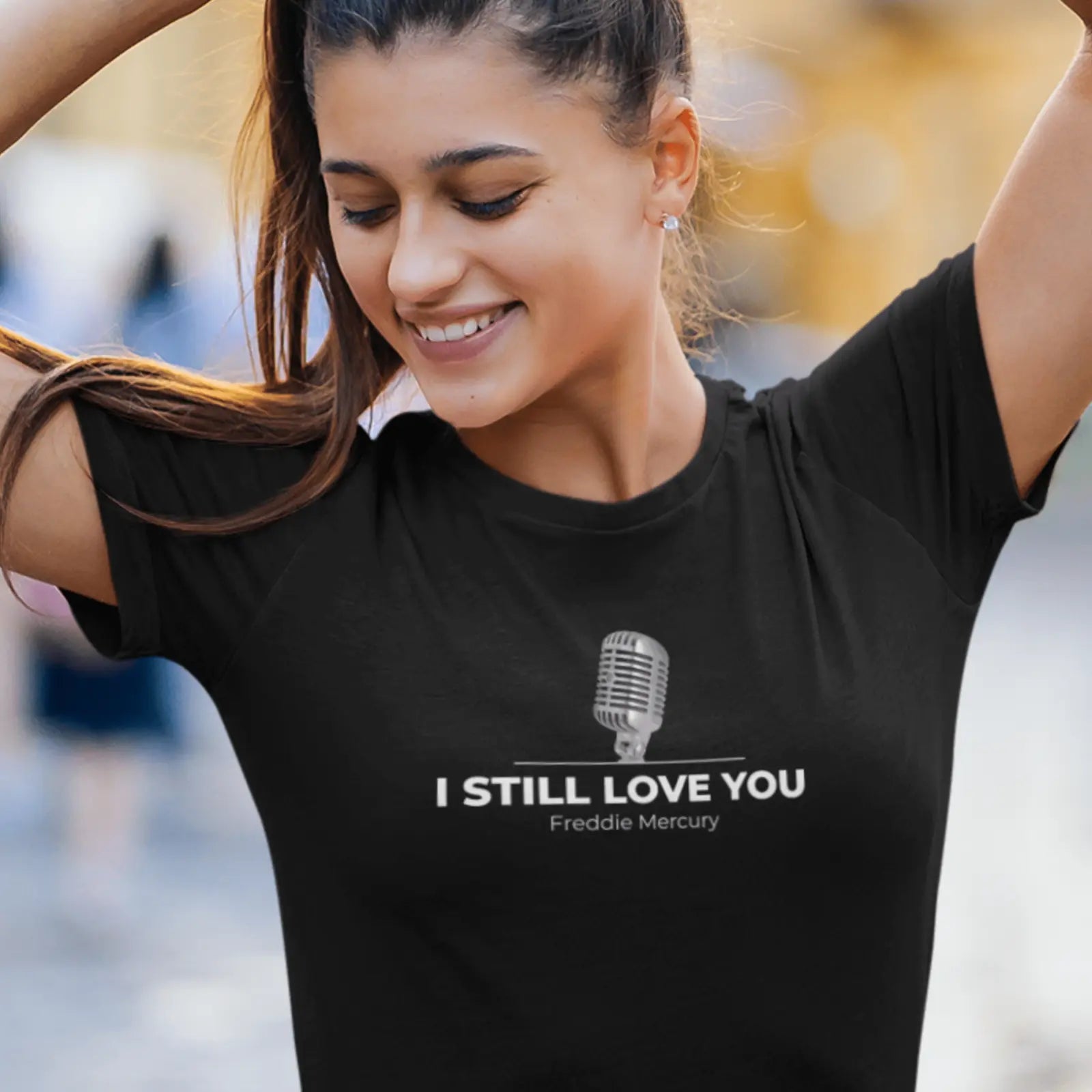 Holka v černém tričku s mikrofonem a nápisem I still love - Freddie Mercury